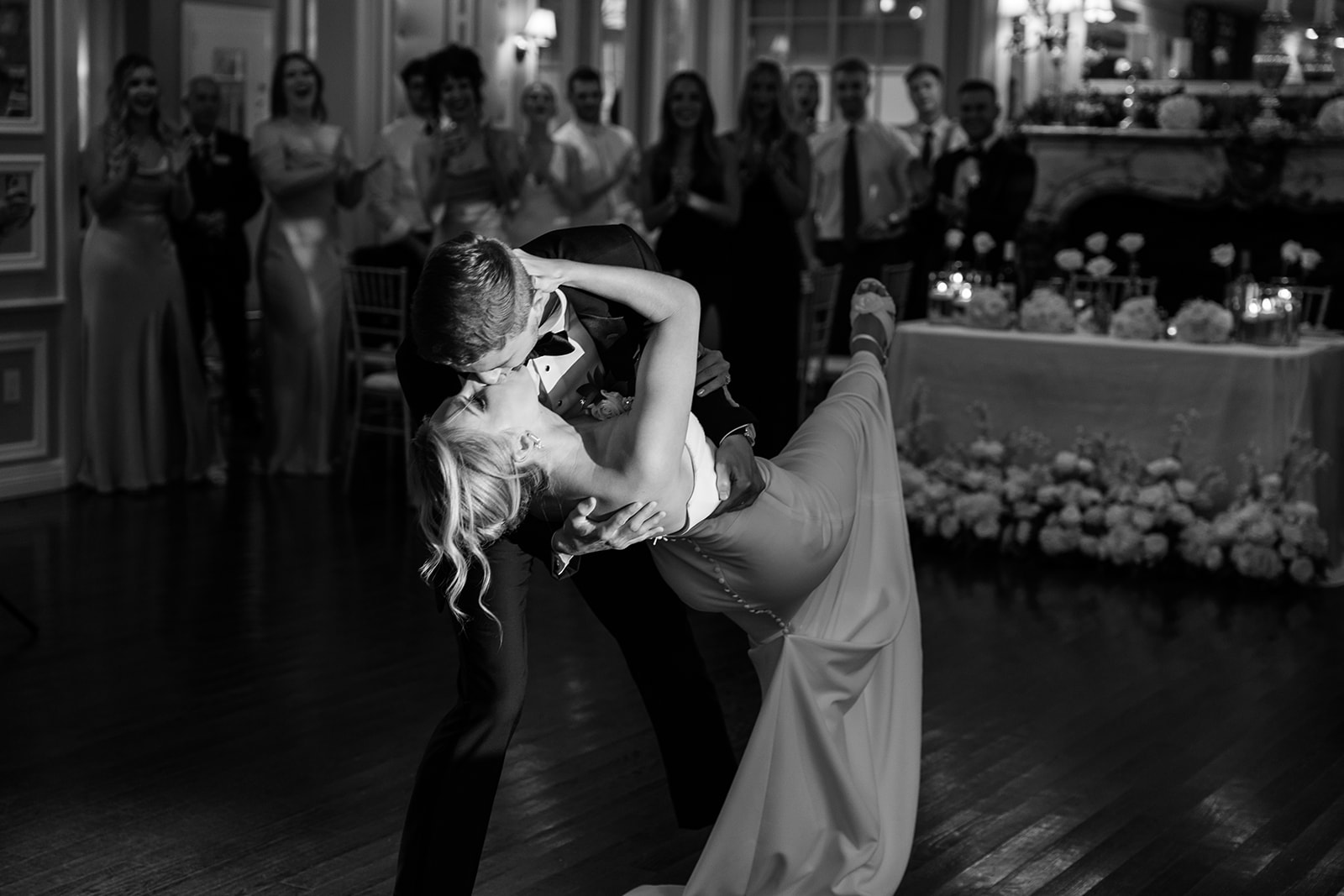 Black and white photo of the groom dipping and kissing the bride, showing a dramatic lift during their first dance.
